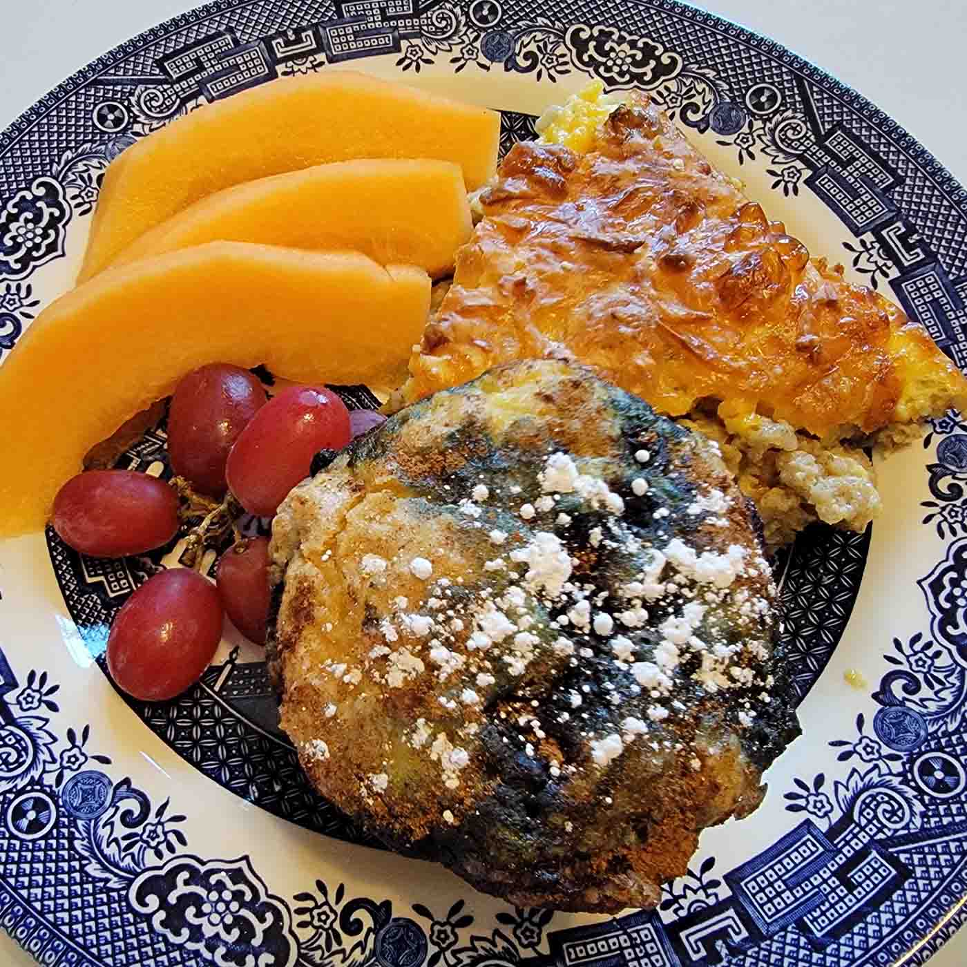 Breakfast plate with fruit, eggs, and a slice of blueberry bake.