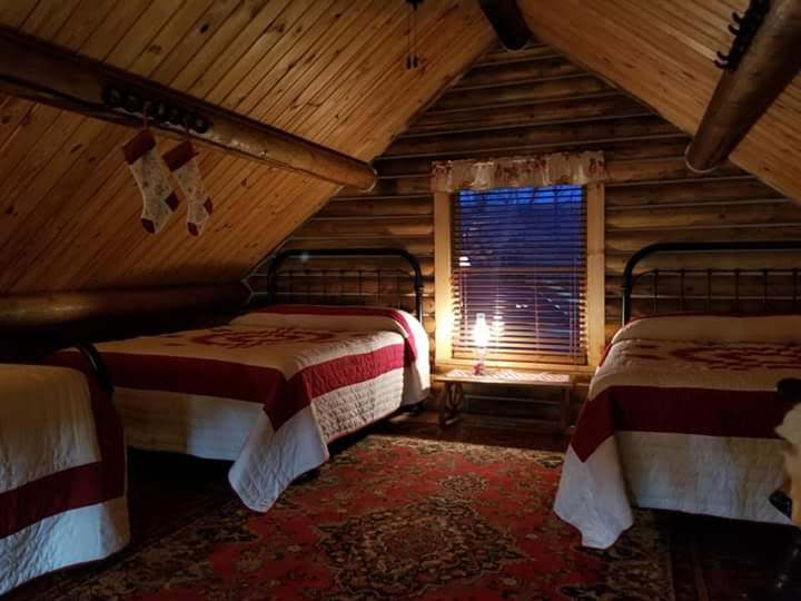 triangle-ranch-cabin-under-the-hill-3 Cozy attic-style guest room with two twin beds and warm wood-paneled ceiling.