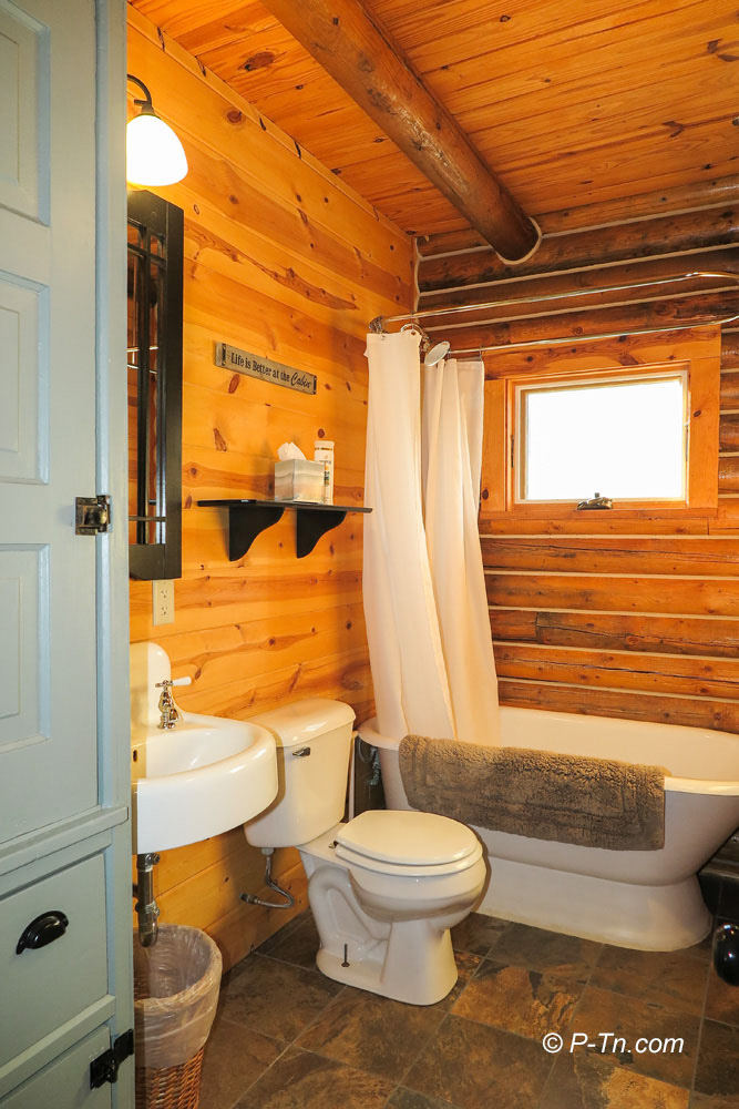 triangle-ranch-cabin-under-the-hill-4 Bathroom with wooden walls, mirror, and tub.