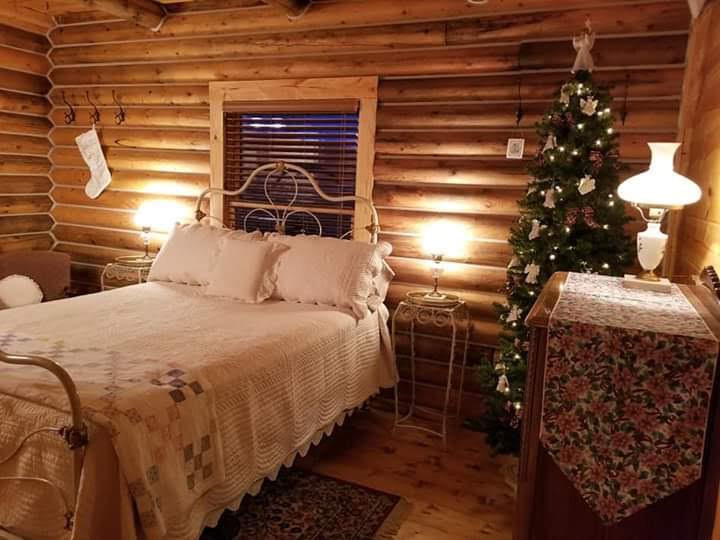 triangle-ranch-cabin-under-the-hill-8 Log-walled bedroom with quilted bed and Christmas tree decor.
